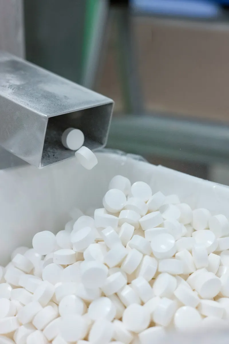Chewable tablets dropping from a compression line into a bin at Adept